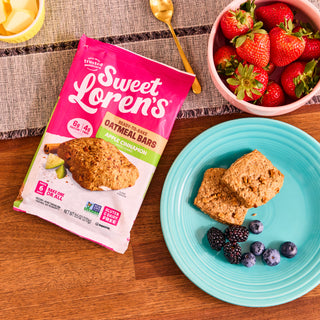 Baked Apple Cinnamon Oatmeal Bars on a plate next to the Sweet Loren's package and fresh berries